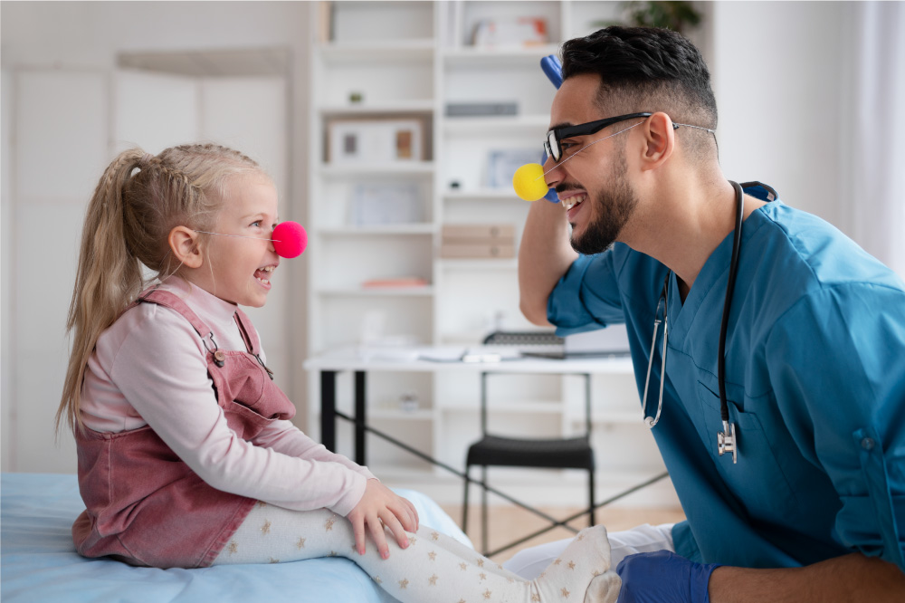 A pediatrician entertains his young patient with a pink clown nose at an appointment. Preparing children for medical appointments helps ease their worries and is a solid step in ensuring they have a positive and comfortable experience.