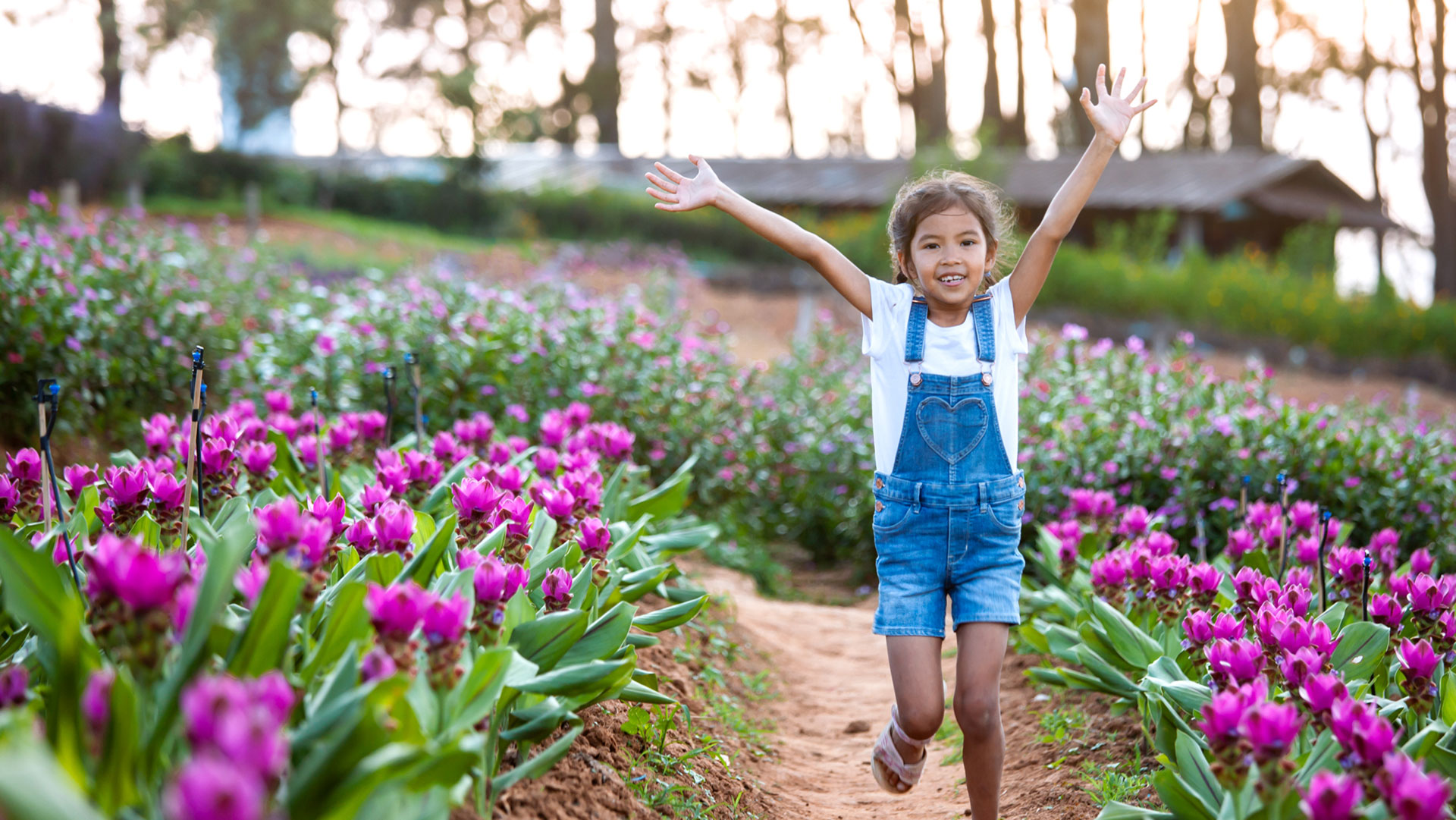 Smiling young girl in denim overalls and a white tee shirt runs joyfully through a spring flower field surrounded by blooming purple tulips—capturing the spirit of outdoor family fun in Portland, Oregon.