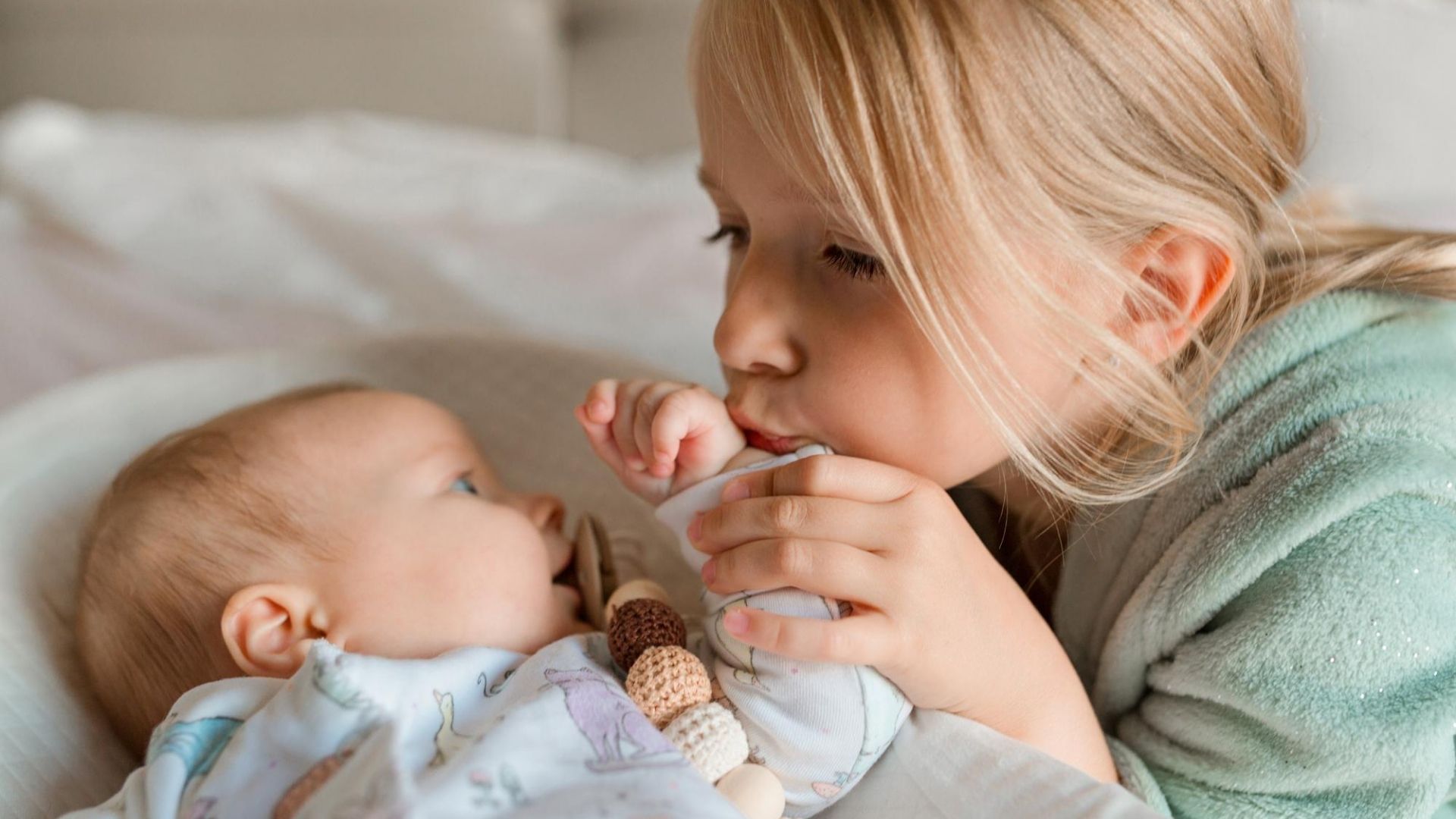Older sister gently kisses her baby sibling’s hand while cuddling together, symbolizing care and protection, key themes in pediatric health and vaccination.